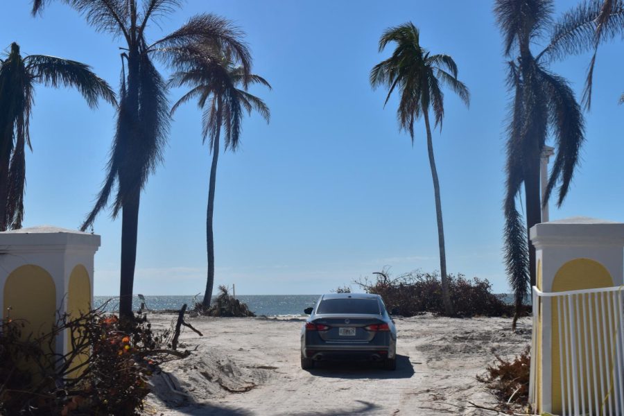 An abandoned car sits isolated on the beach, just past what used to be a visible parking lot.