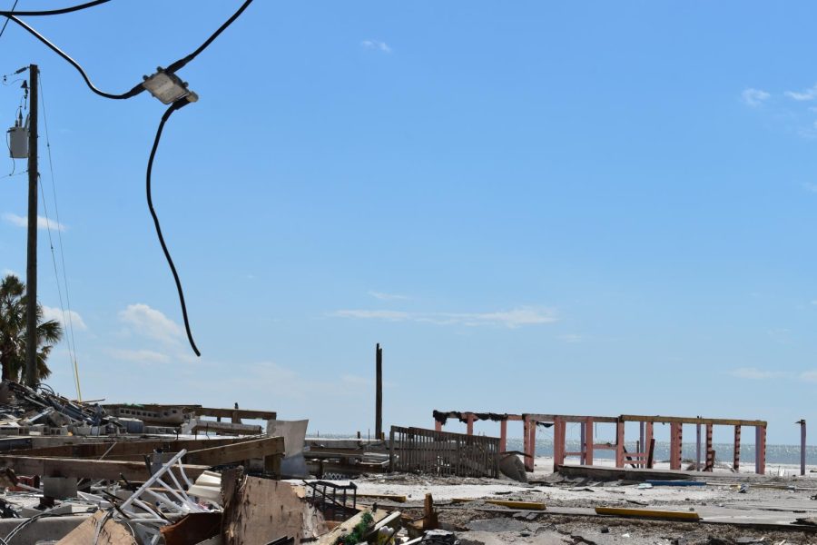 A disconnected power line hangs above a pile of debris from the hurricane with a frame from what used to be a building standing behind it.