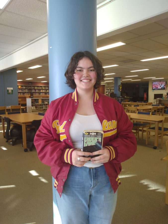 Club member Amara Guss (11) poses with her book recommendation, Orson Scott Cards Enders Game. I think its really just [an] interesting exploration of right and wrong and duty and lies and how they all kind of fit together and its also just really interesting, like futuristic sci-fi kind of world, Guss said.